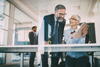 a man wearing a suit and tie talking to a business woman who is showing him something on a tablet